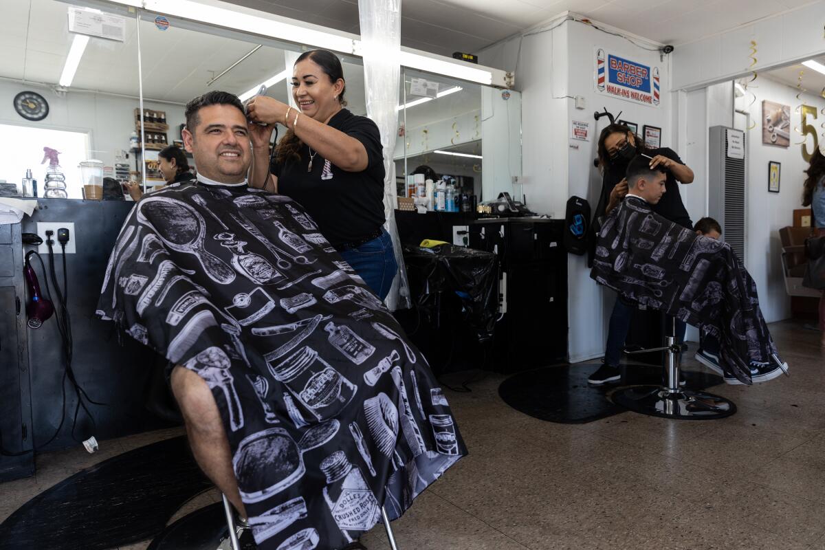 Erica Lora and Socorro Gastelum give haircuts to Jorge Molina and his son Roman,12, at Highland Barber Shop on July 16, 2022.