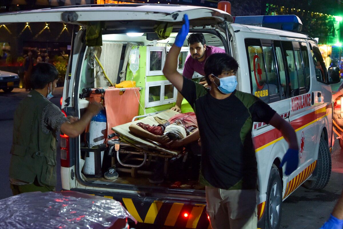 A person with a bandaged head lies on a stretcher in an ambulance with three medical workers nearby