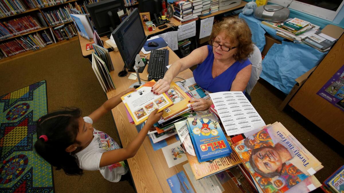 Samantha Hernandez, 8, left, checks out a book in May from library aide Nina Briggs at Meyler Street Elementary School in West Carson. Briggs won't lose her job but 30 other Los Angeles Unified library aides are targeted for layoffs.