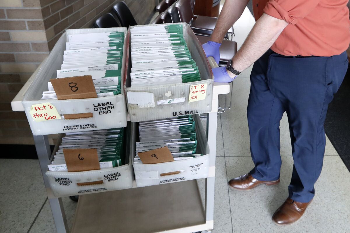 FILE - In this May 5, 2020, file photo, Jordan Smellie moves absentee ballots to be counted at City Hall in Garden City, Mich. The Michigan appeals court has denied a request to require the counting of absentee ballots received after the time polls close on Election Day. The ruling says the deadline remains intact despite voters' approval of a constitutional amendment that expanded mail-in voting. (AP Photo/Paul Sancya, File)