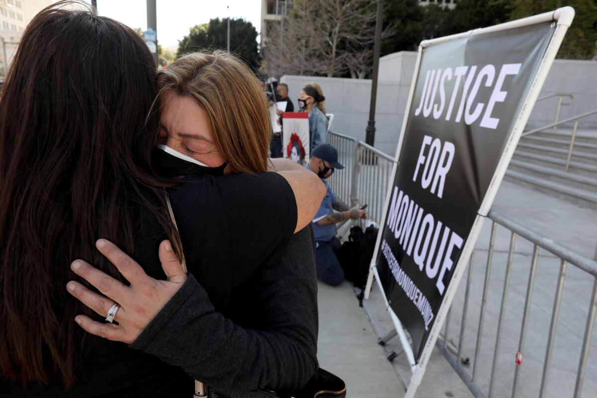 Two women hug near a sign that reads "Justice for Monique."