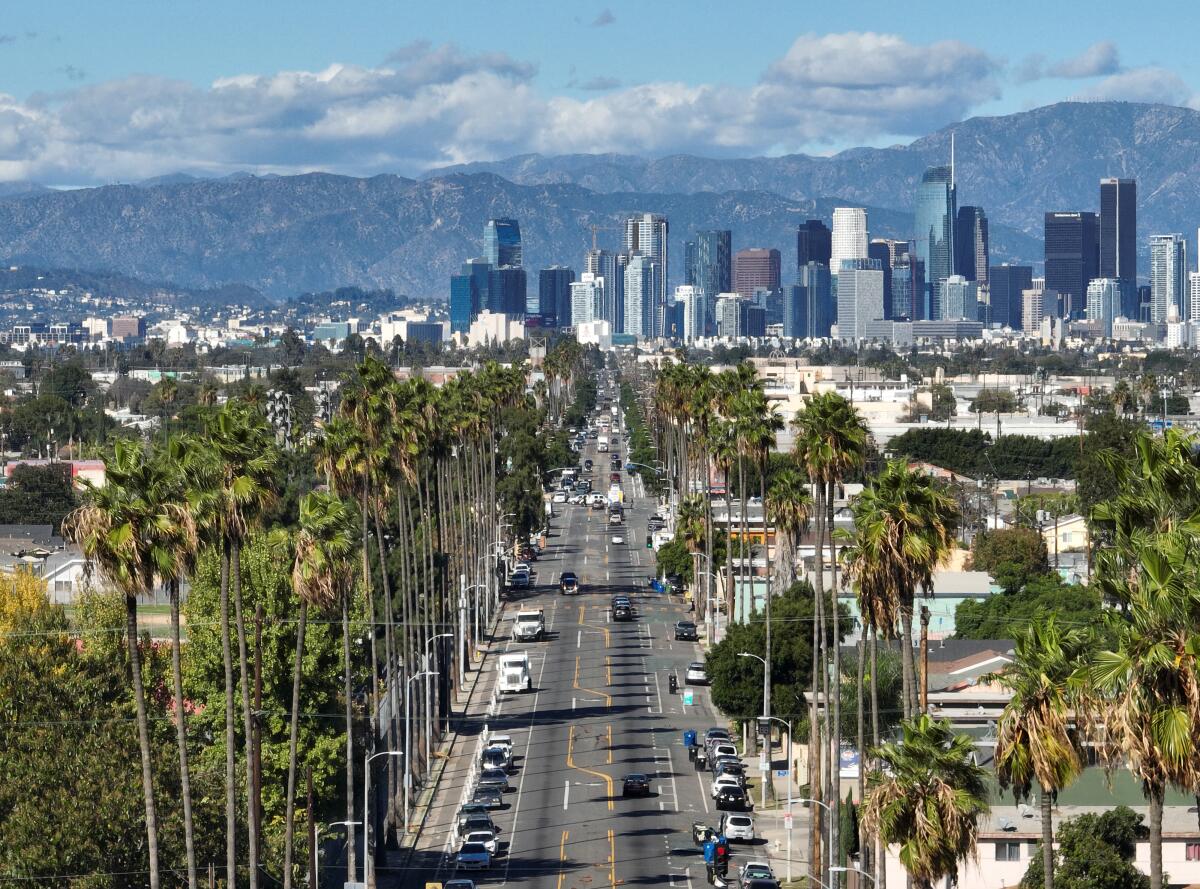 A long street leads toward a city skyline and mountains beyond