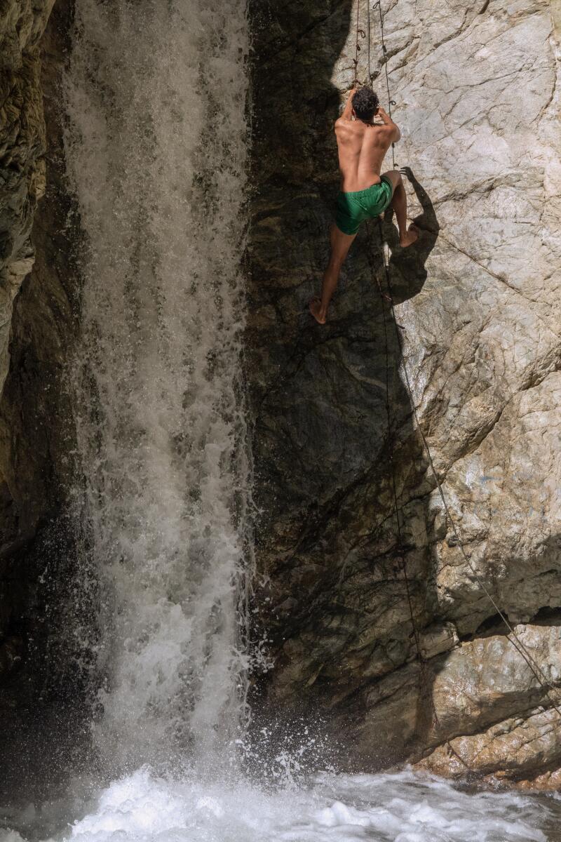 A visitor uses a rope to climb up a section of Stoddard Canyon Falls before jumping into the pool.