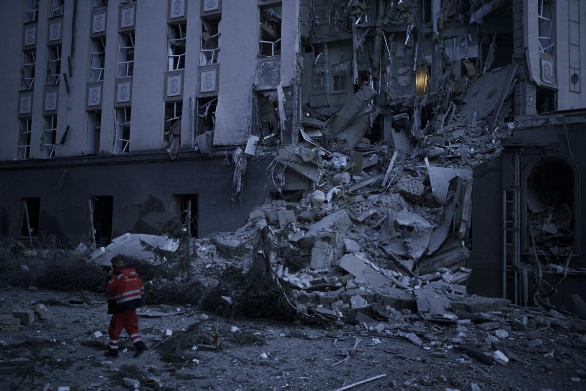 An emergency worker walks past a huge pile of debris spilling from a damaged building.