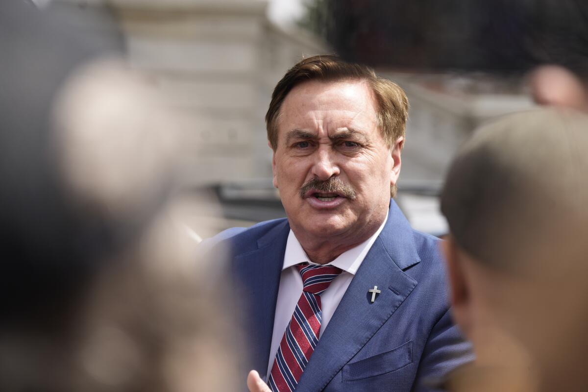 Mike Lindell in a blue suit with a silver crucifix on a lapel.