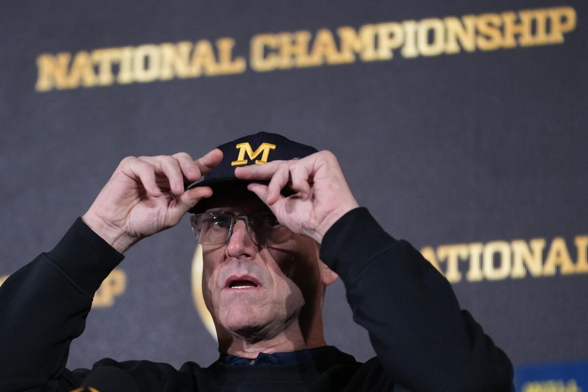 Michigan head coach Jim Harbaugh adjusts his cap before a press conference.