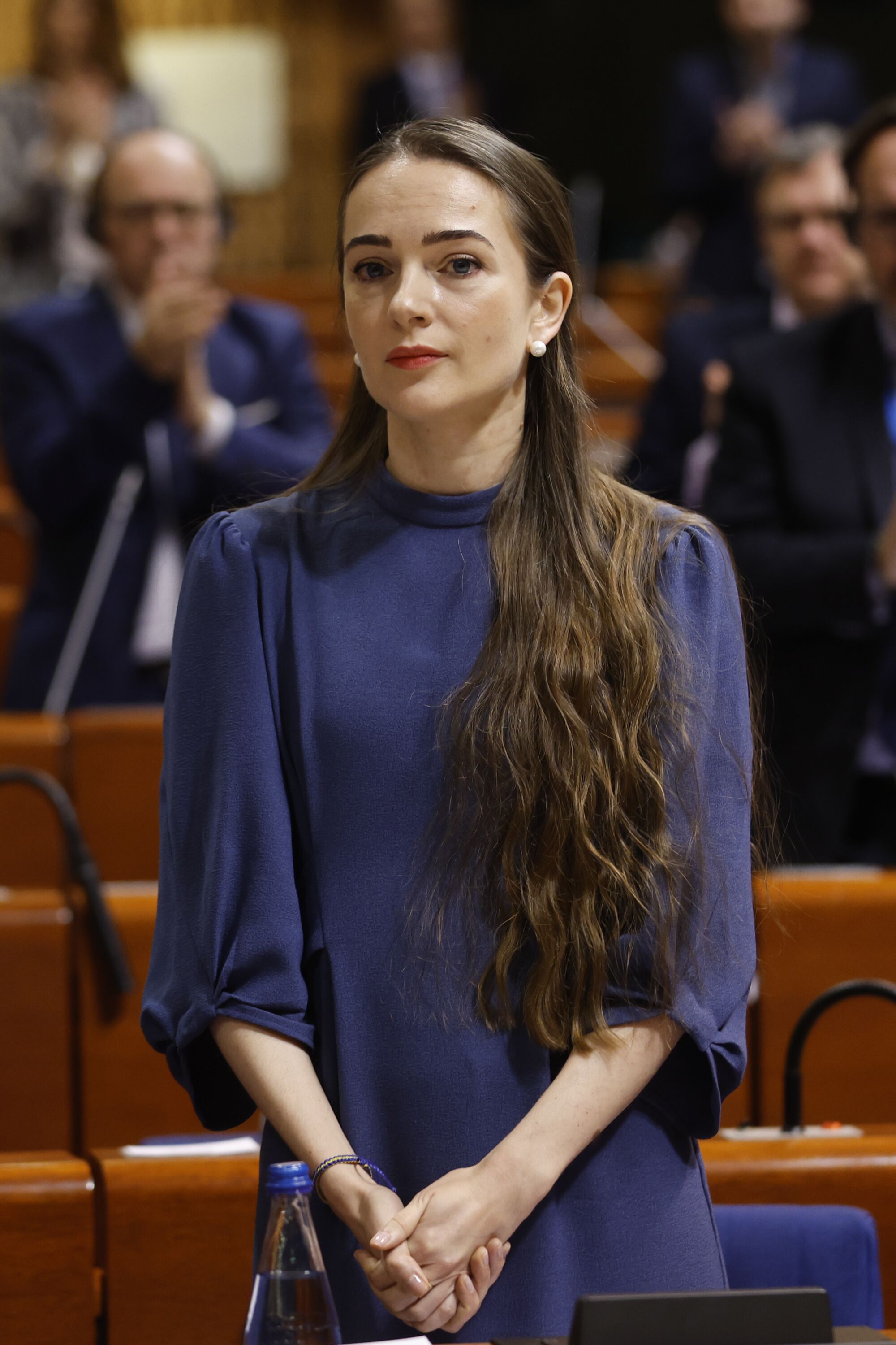 Oleksandra Matviichuk, uzun saçlarını omzunun üzerinden öne doğru toplamış ve ellerini önünde kavuşturmuş halde duruyor.