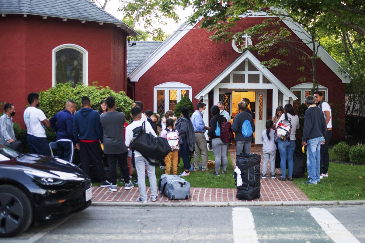 Knots of people standing on a lawn and brick sidewalk outside a small church 