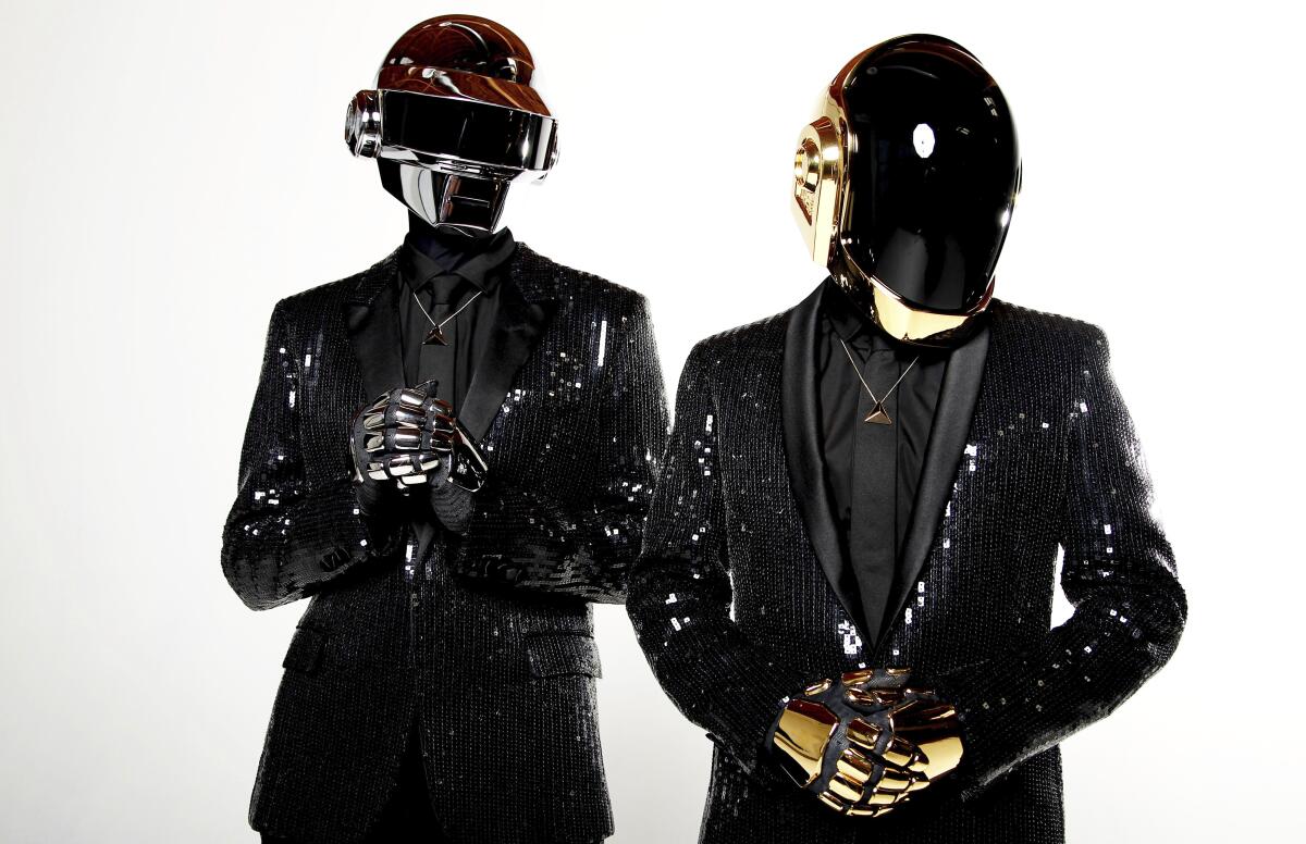 Two men dressed in robot helmets and shiny suits.