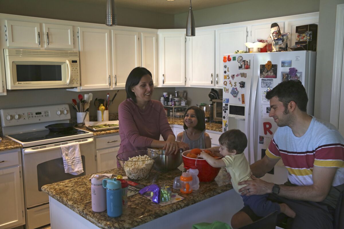 Katherine Rutigliano prepares a meal with her husband, Elio, right, along with their son, Theo, and daughter, Charlotte, at their home in Phoenix, Ariz., on March 16, 2020. When the couple moved away from San Francisco in 2013, they figured they would never meet a fellow Democrat again. Rutgliano didn't realize it, but she had moved her family to what is now the front lines in American politics. (AP Photo/Dario Lopez-Mills)