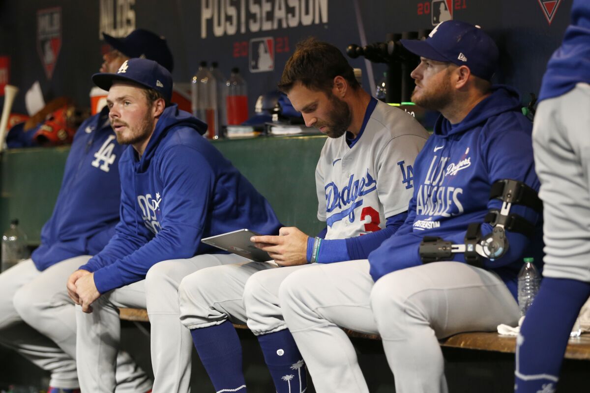 Injured Dodgers first baseman Max Muncy sits in the dugout next to Gavin Lux and Chris Taylor.