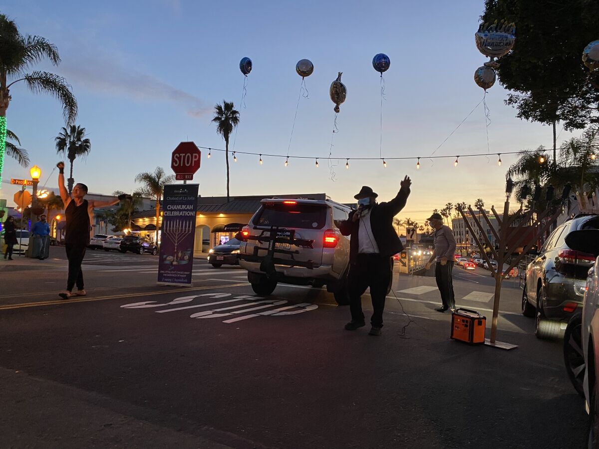 Rabbi Baruch Ezagui, center, speaking against a backdrop of Hanukkah balloons and a fire dancer.