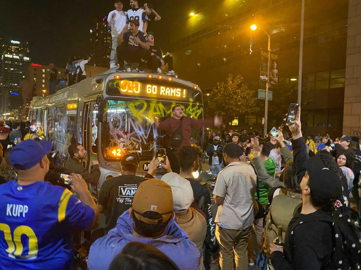 Rams fans pose on top of and in front of a Los Angeles Metro bus with a sign that reads “Go Rams!”.