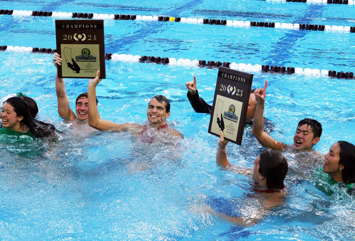 The Costa Mesa High boys' swim team jumps in the pool holding its 2023 and 2024 title plaques.