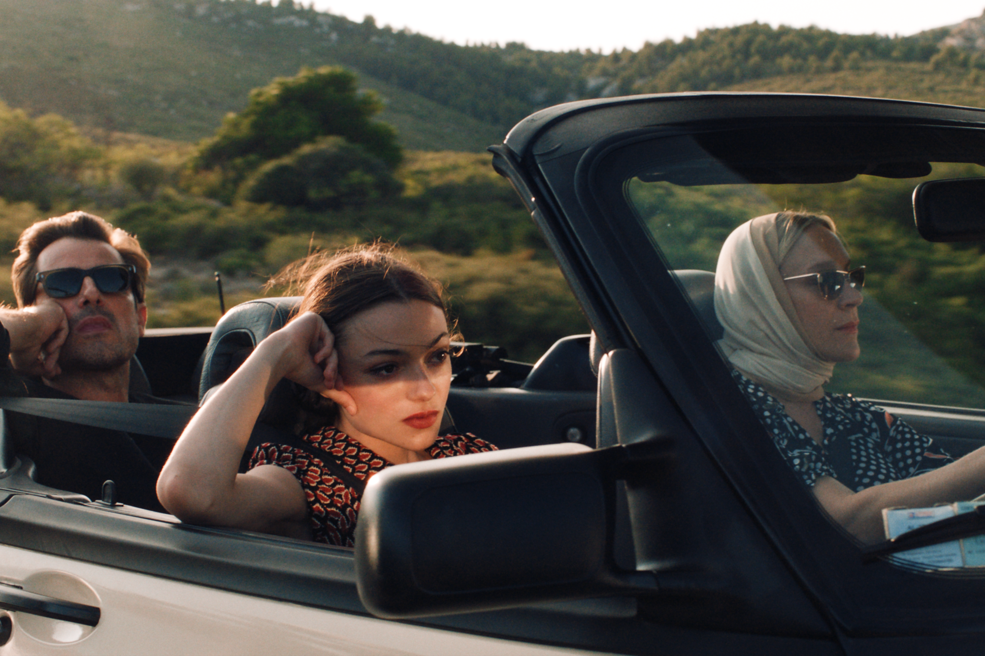 Three people in shades drive in a convertible.