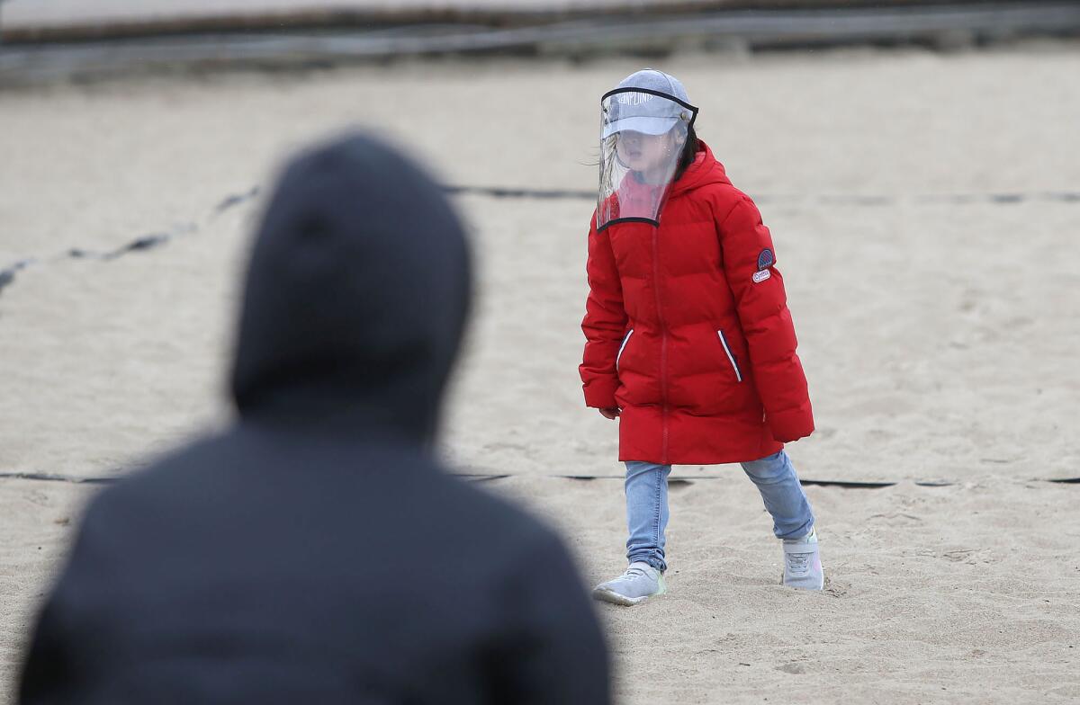 Grace Tanaka wears a protective face shield as she walks on empty Main Beach volleyball courts in Laguna Beach on Monday. City beaches are being closed in an effort to curb the spread of the COVID-19 coronavirus.