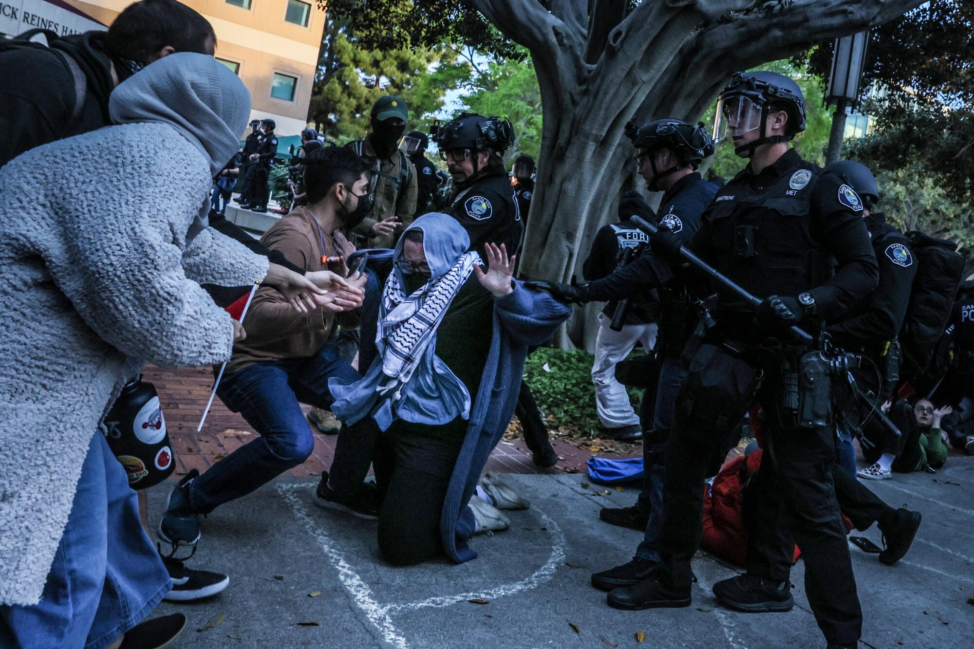 Police grab a kneeling protester as they break up a demonstration at UC Irvine.