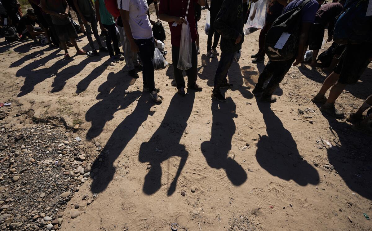 A line of people, with shadows thrown on the dusty ground. 