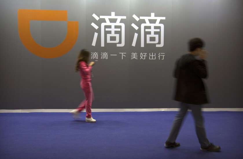 FILE - In this April 27, 2017, file photo, visitors walk past a sign for Chinese ride-hailing service Didi Chuxing at the Global Mobile Internet Conference (GMIC) in Beijing. Chinese ride-hailing service Didi says it lost $5.5 billion over the past three years ahead of its U.S. stock market debut Wednesday, June 30, 2021, but it's highlighting its global reach and investments in developing electric and self-driving cars. (AP Photo/Mark Schiefelbein,File)