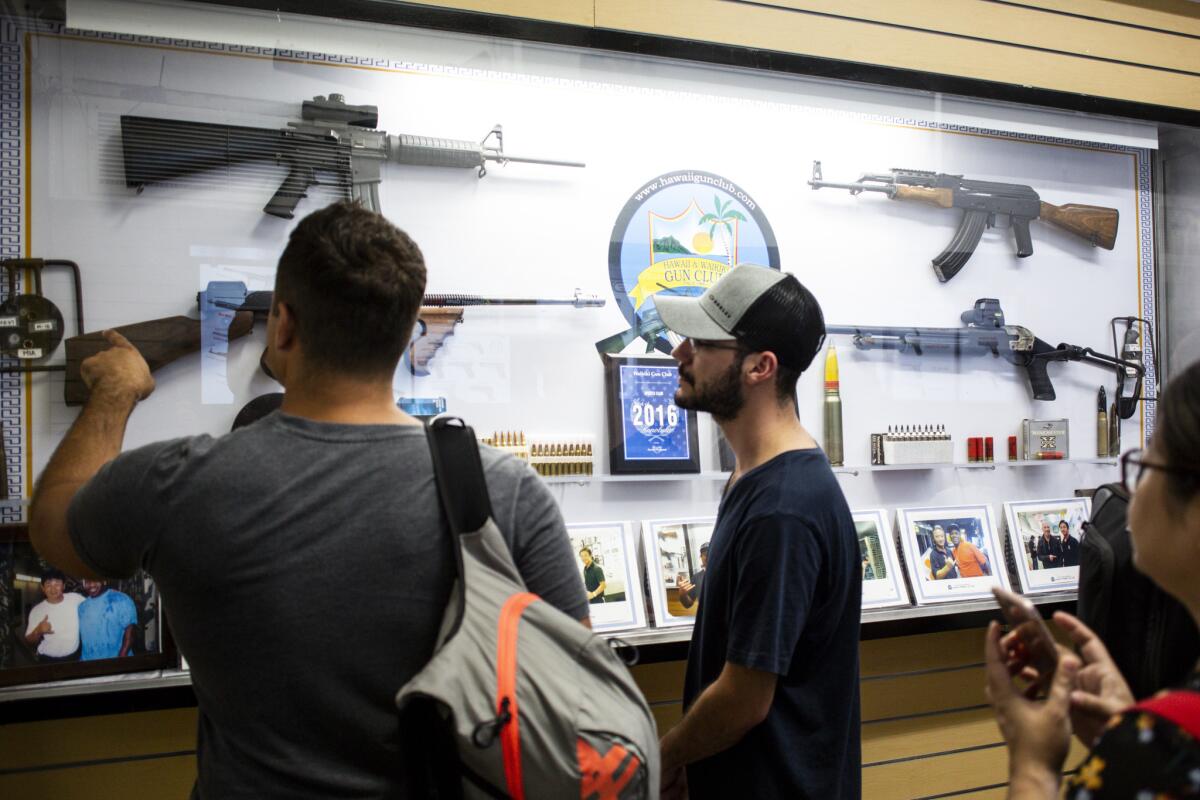While waiting to pay for a shooting session, Oliver Girard, left, from Canada and Marcus Axisa, center, from Australia look at firearms on display in the lobby of the Waikiki Gun Club in Honolulu.