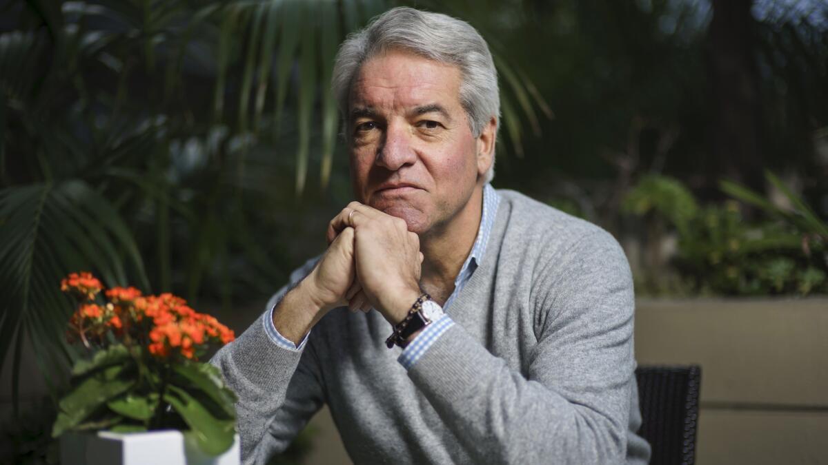 Andy King sits with his hands folded beneath his chin in a gray sweatshirt and blue checkered shirt