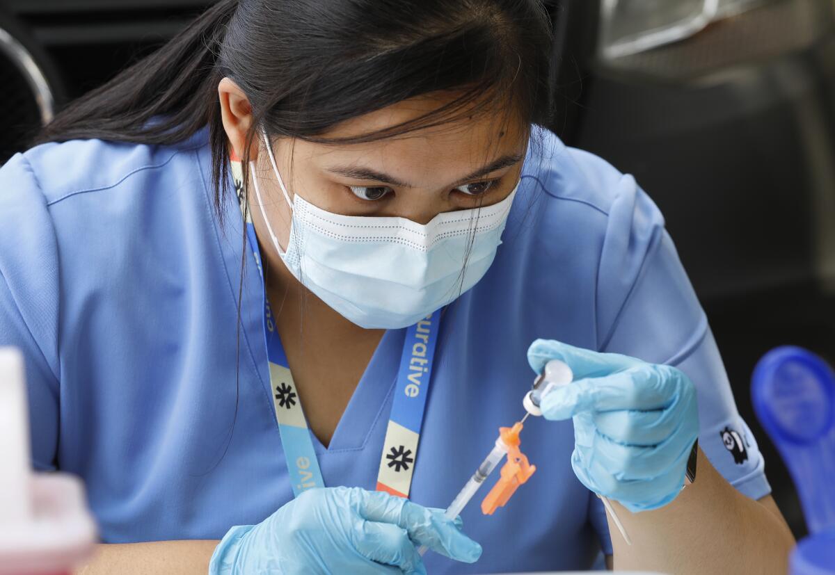 a nurse wearing a face mask prepares a COVID vaccine