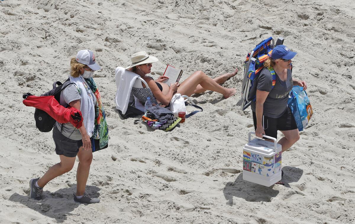 Beachgoers walk across the sand looking for a spot to post their chairs while another reads a book.