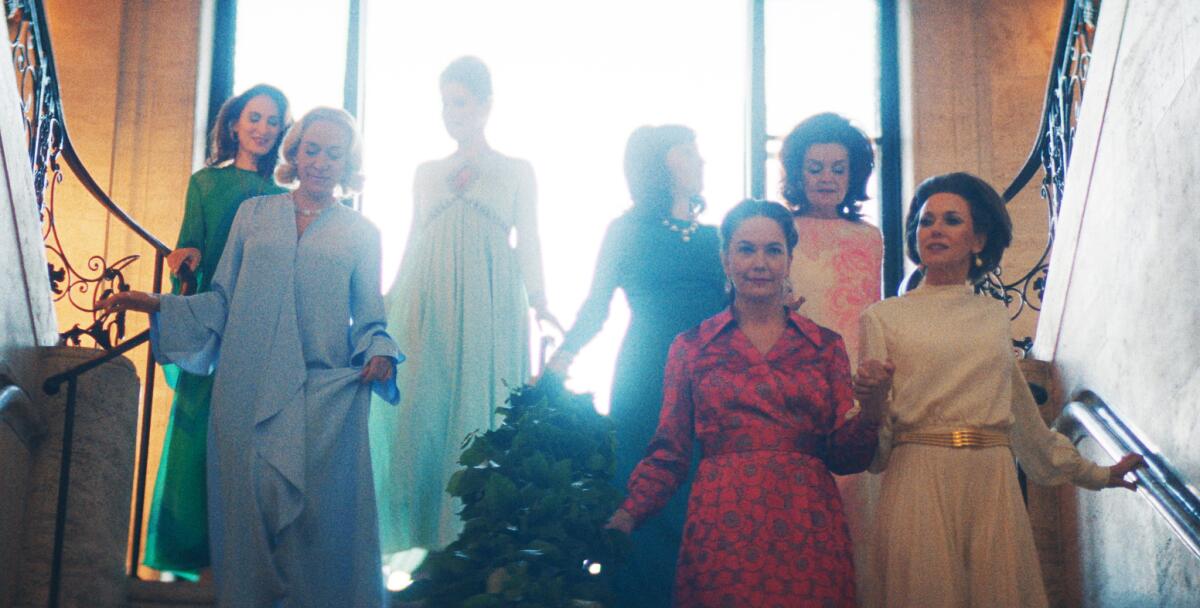 A group of women in 1980s-style dresses descends a staircase.