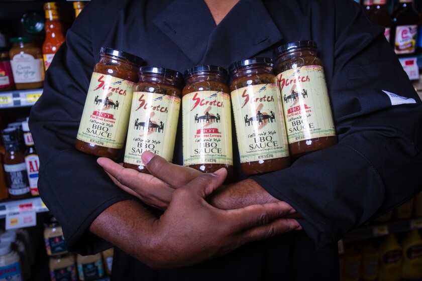 Closup of Antonio Mays arms holding five jars of his company's barbecue sauce in original and spicy flavors.