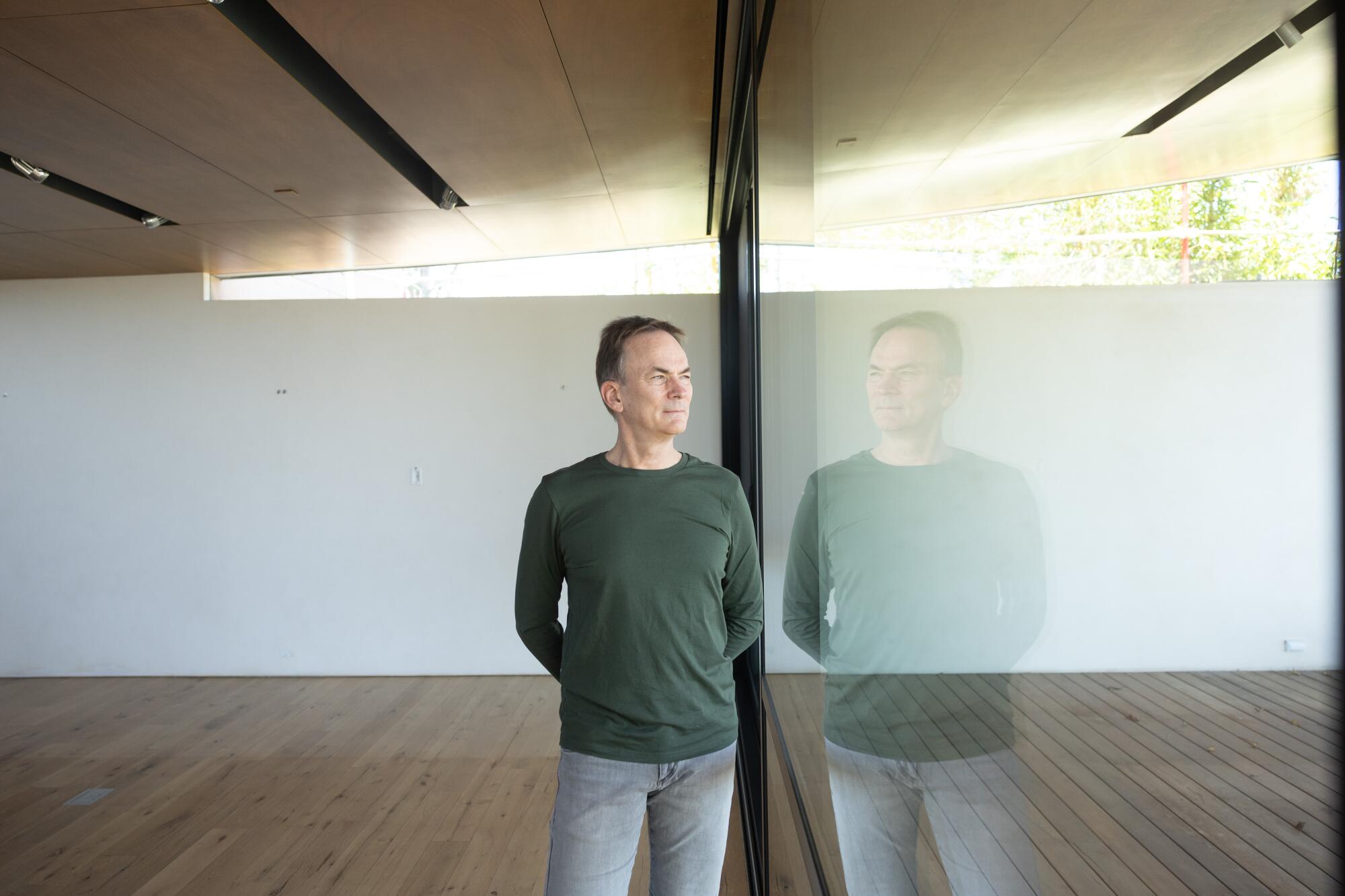 A man stands next to a window that shows his reflection.