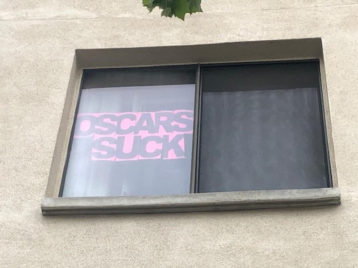 A pink sign in an apartment window says "Oscars Suck."