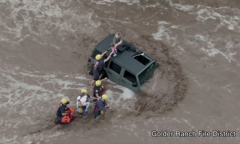 This drone image provided by the Golder Ranch Fire District shows firefighters safely rescue a man and his two daughters from the roof of their vehicle after it was swept away in fast moving water just north of Tucson, Ariz., on Wednesday, July 14, 2021. (Golder Ranch Fire District via AP)