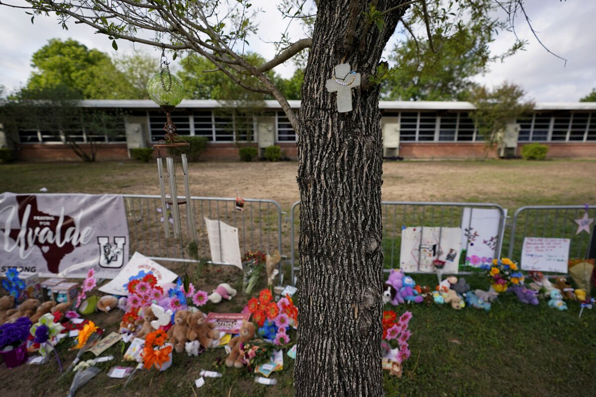 FILE - A cross hangs on a tree at Robb Elementary School on June 3, 2022, in Uvalde, Texas, where a memorial has been created to honor the victims killed in the recent school shooting. Two teachers and 19 students were killed. As public pressure mounts for more information on the deadly Uvalde school shooting, some are concerned that Texas officials will use a legal loophole to block records from being released — even to the victims' families — once the case is closed.(AP Photo/Eric Gay, File)