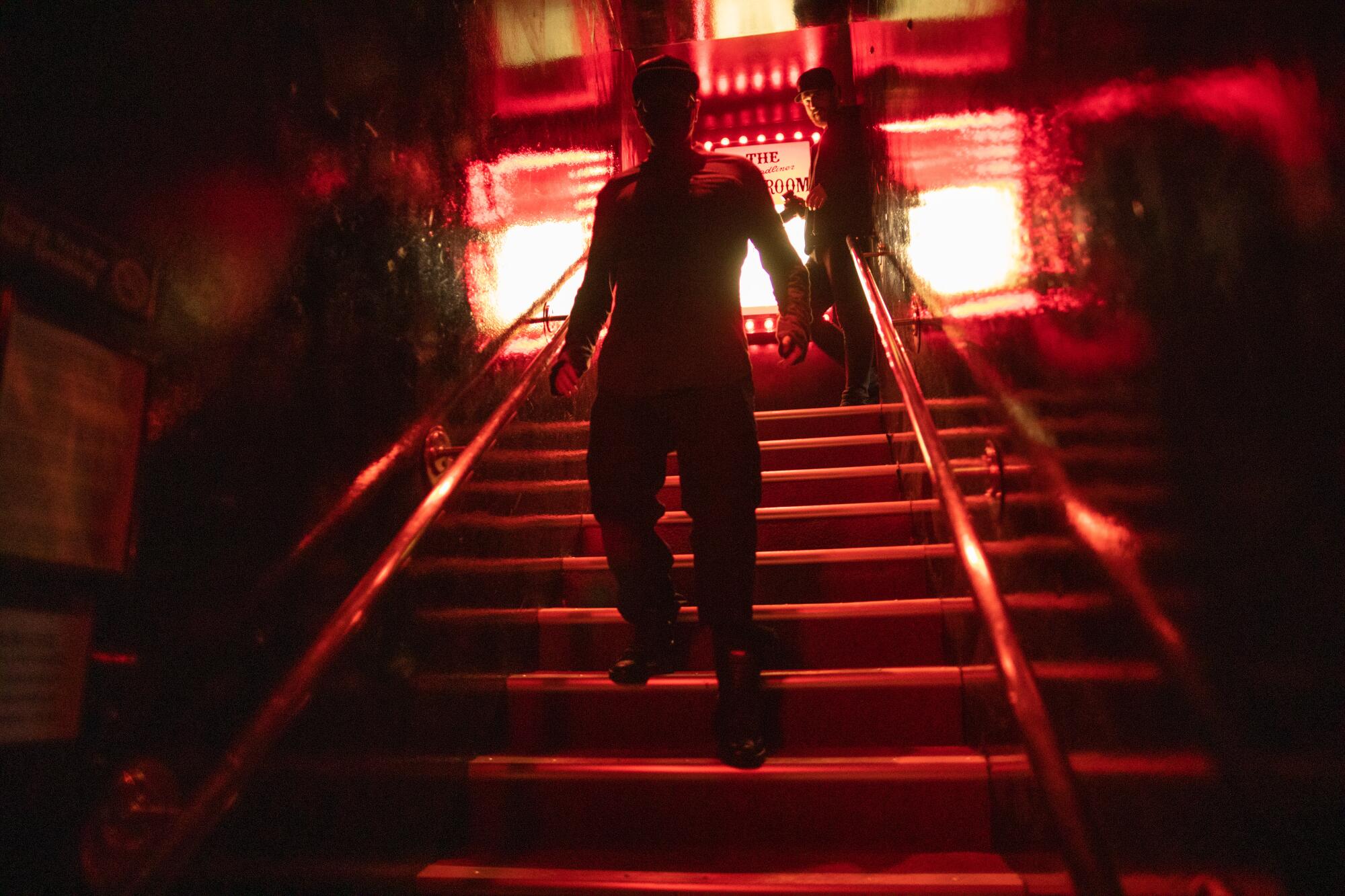 silhouette of two men walking down stairs in dark and red lighting 
