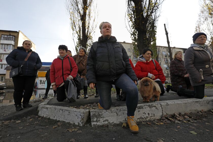 Borodyanka, Ukraine-Nov. 9, 2022-On Nov. 9, 2022, residents of Borodyanka kneel as the casket carrying Oleksii Kozlenko, age 32, proceeds down Tsentralna Street during a procession to the cemetery. He was killed on the frontline in Bakhmut, Ukraine leaving his wife and children behind. (Carolyn Cole / Los Angeles Times)