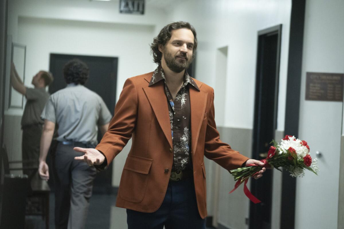 A man in a leisure suit holds flowers in a corridor.