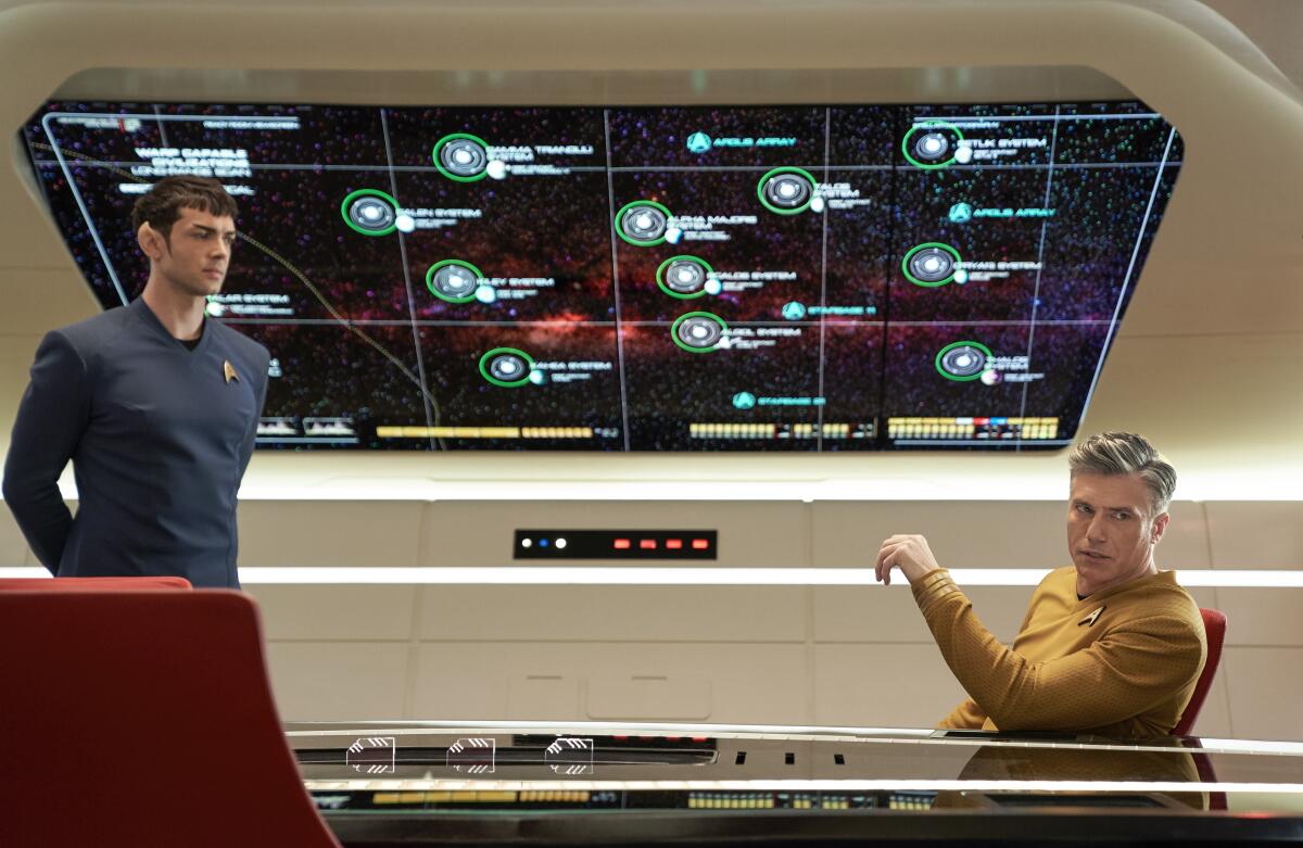 A half-human, half-Vulcan male and a human man in the control room of a spaceship