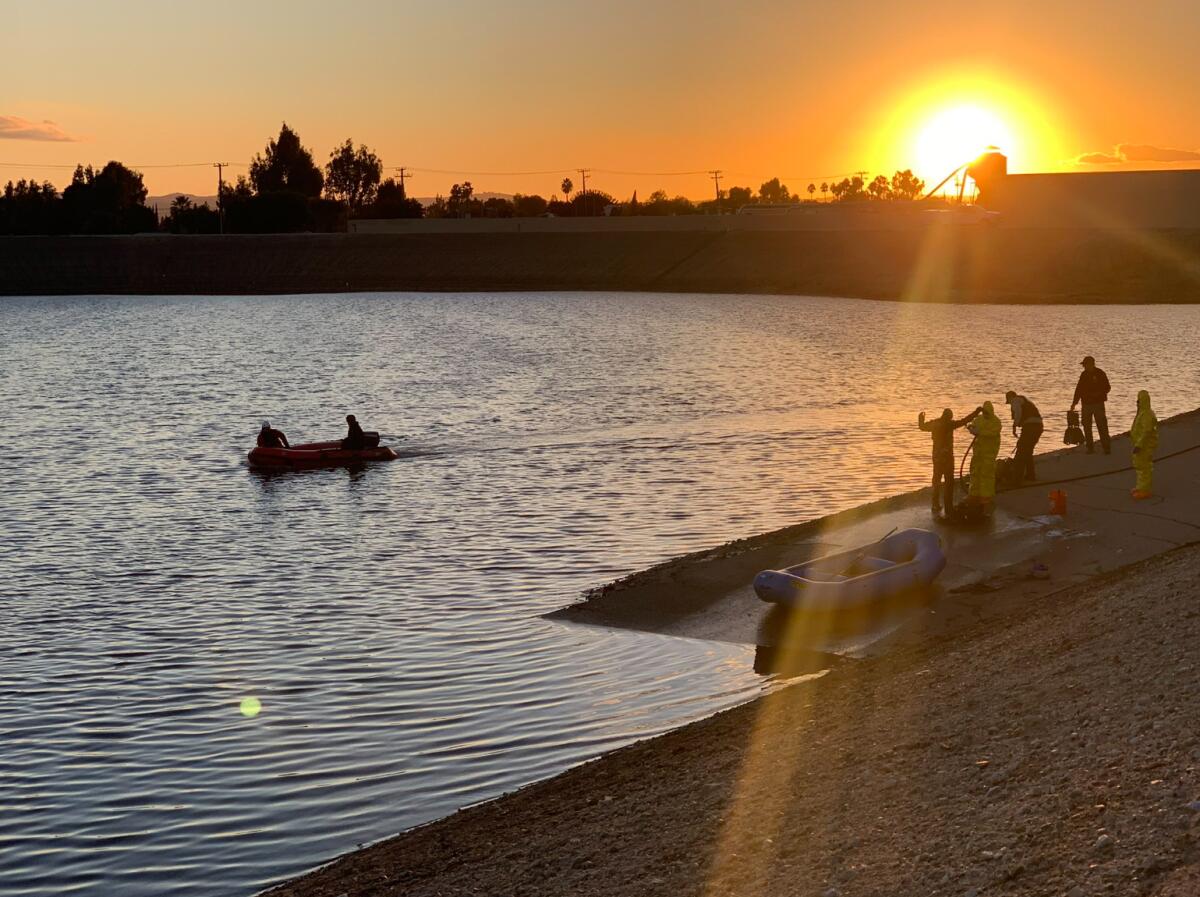 Two people in a raft in a flood channel as several others stand on the shore nearby