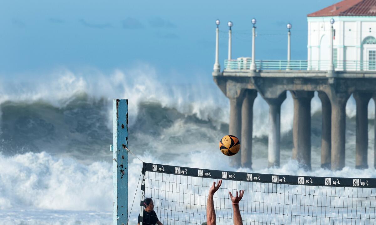 Beach volleyball players compete in a tournament as high waves crash against a pier