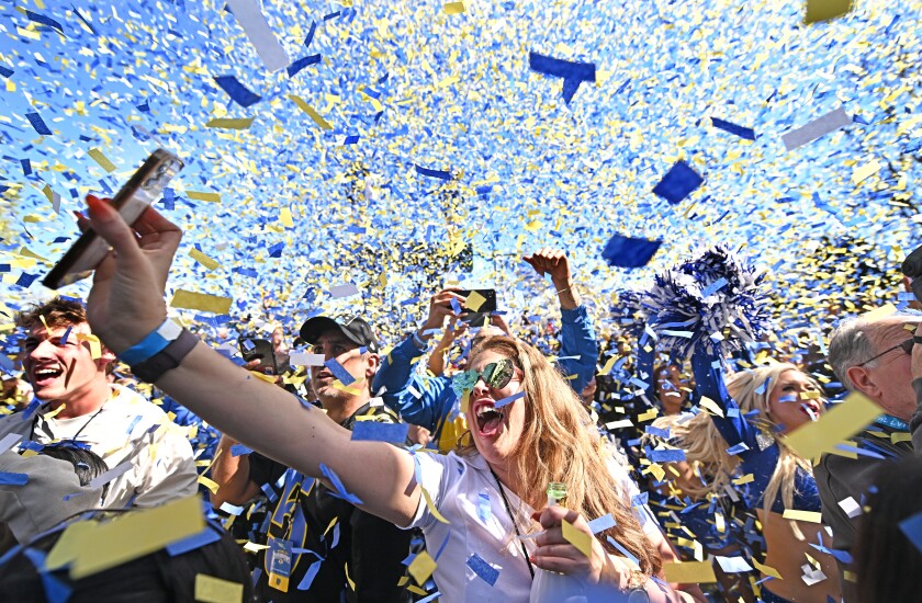 Unmasked people in a crowd shout amid a hail of confetti.