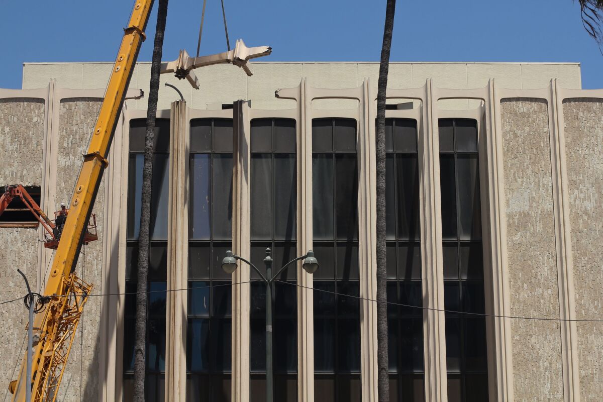 A massive construction crane is seen removing a fragment of LACMA's columnar façade.