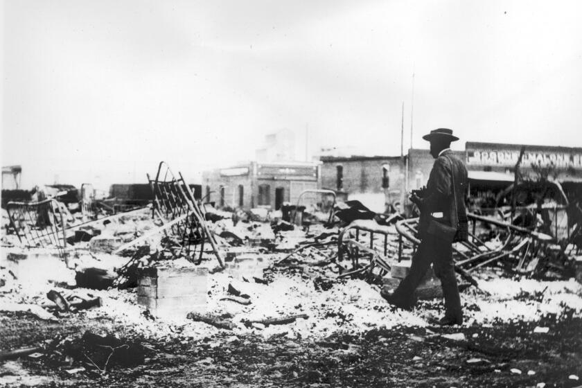 Photograph of an African-American man with a camera looking at the skeletons of iron beds which rise above the ashes of a burned-out block after the Tulsa Race Riot, Tulsa, Oklahoma, 1921. (Photo by Oklahoma Historical Society/Getty Images)