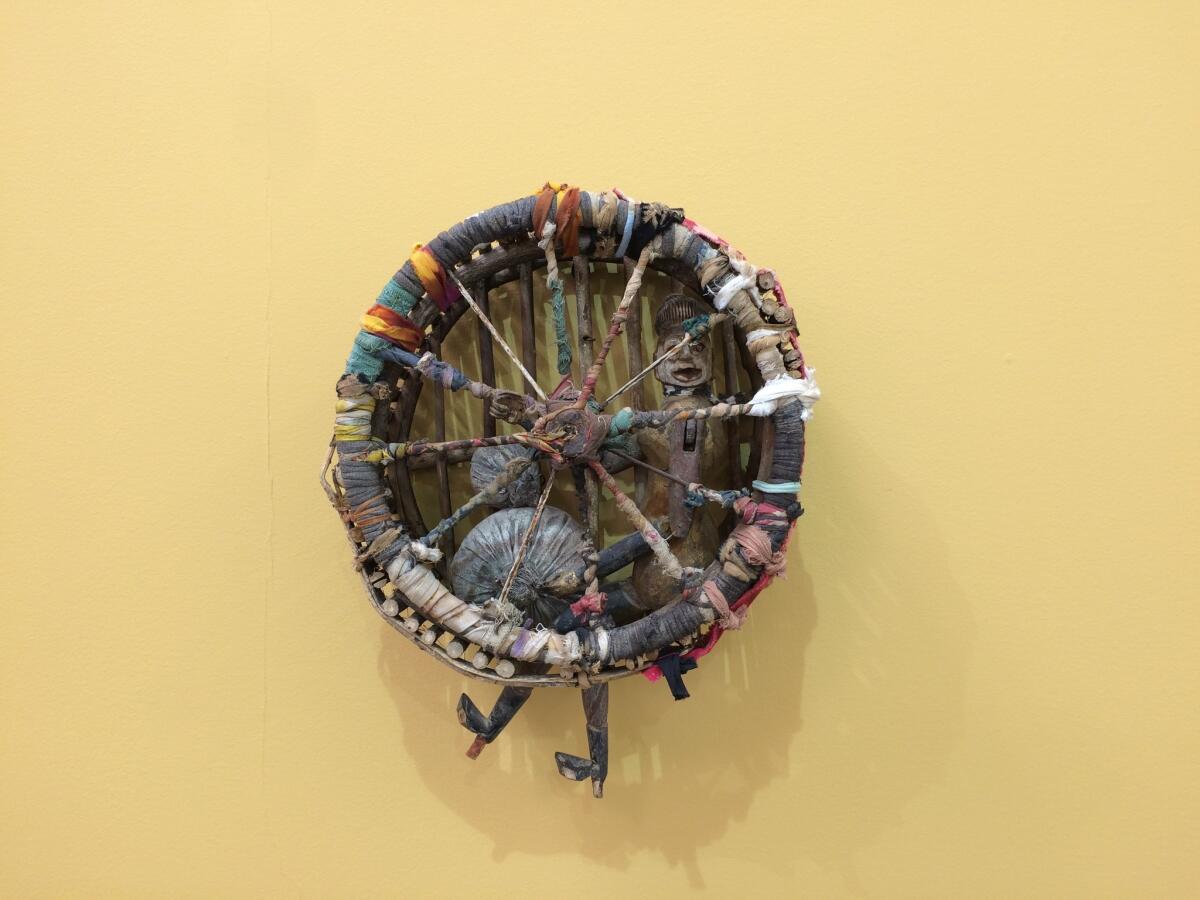 A figure sits inside a wheel made of wood and rags in the 2008 sculpture "Caged."