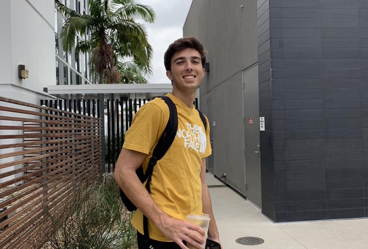 A smiling Dylan Hernandez stands on campus wearing a backpack.