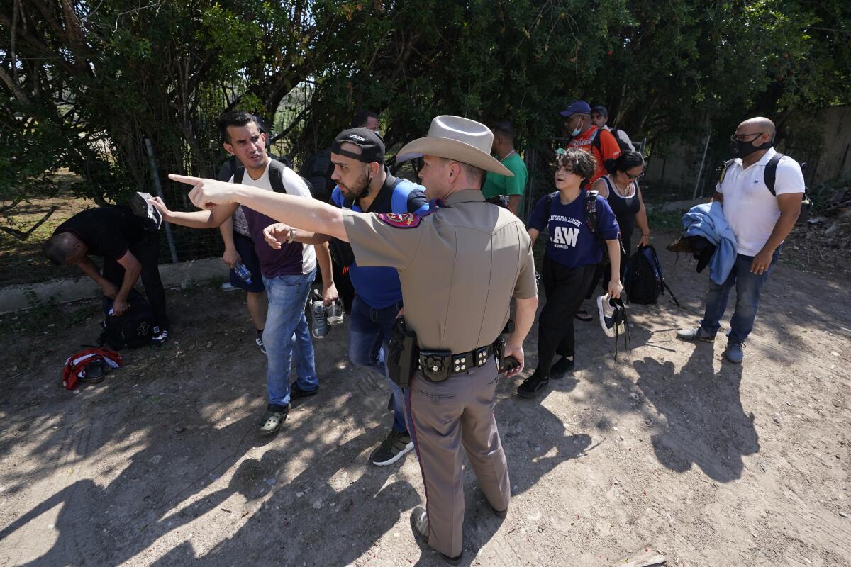 FILE - In this Wednesday, June 16, 2021 file photo, A Texas Department of Public Safety officer in Del Rio, Texas directs a group of migrants who crossed the border and turned themselves in. he Biden administration sued Texas on Friday, July 30, 2021 to prevent state troopers from stopping vehicles carrying migrants on grounds that they may spread COVID-19, warning that the practice would exacerbate problems amid high levels of crossings on the state's border with Mexico. (AP Photo/Eric Gay, File)