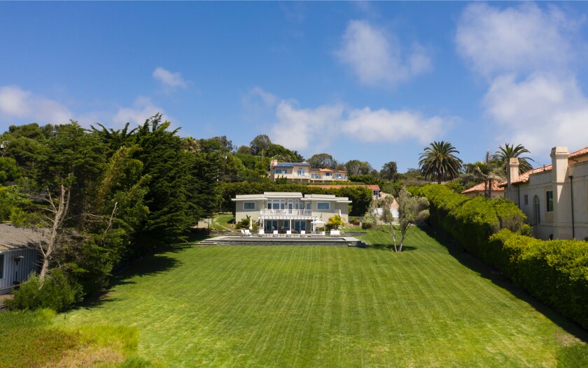 The scenic property holds a two-story home and a rolling lawn that descends toward the sand.