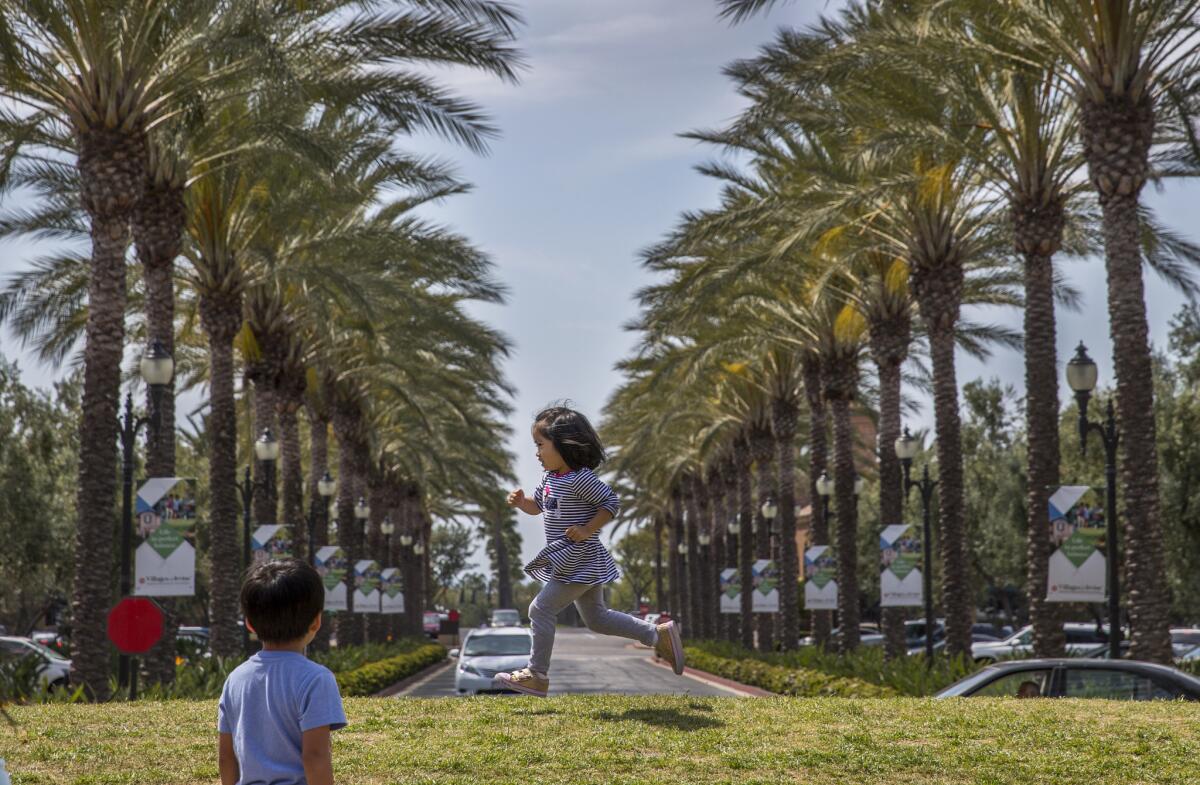 Kate Claribel, 3, whose parents just bought a home in Irvine, plays with other kids in the grass along a street lined with palm trees at the Woodbury Town Center.