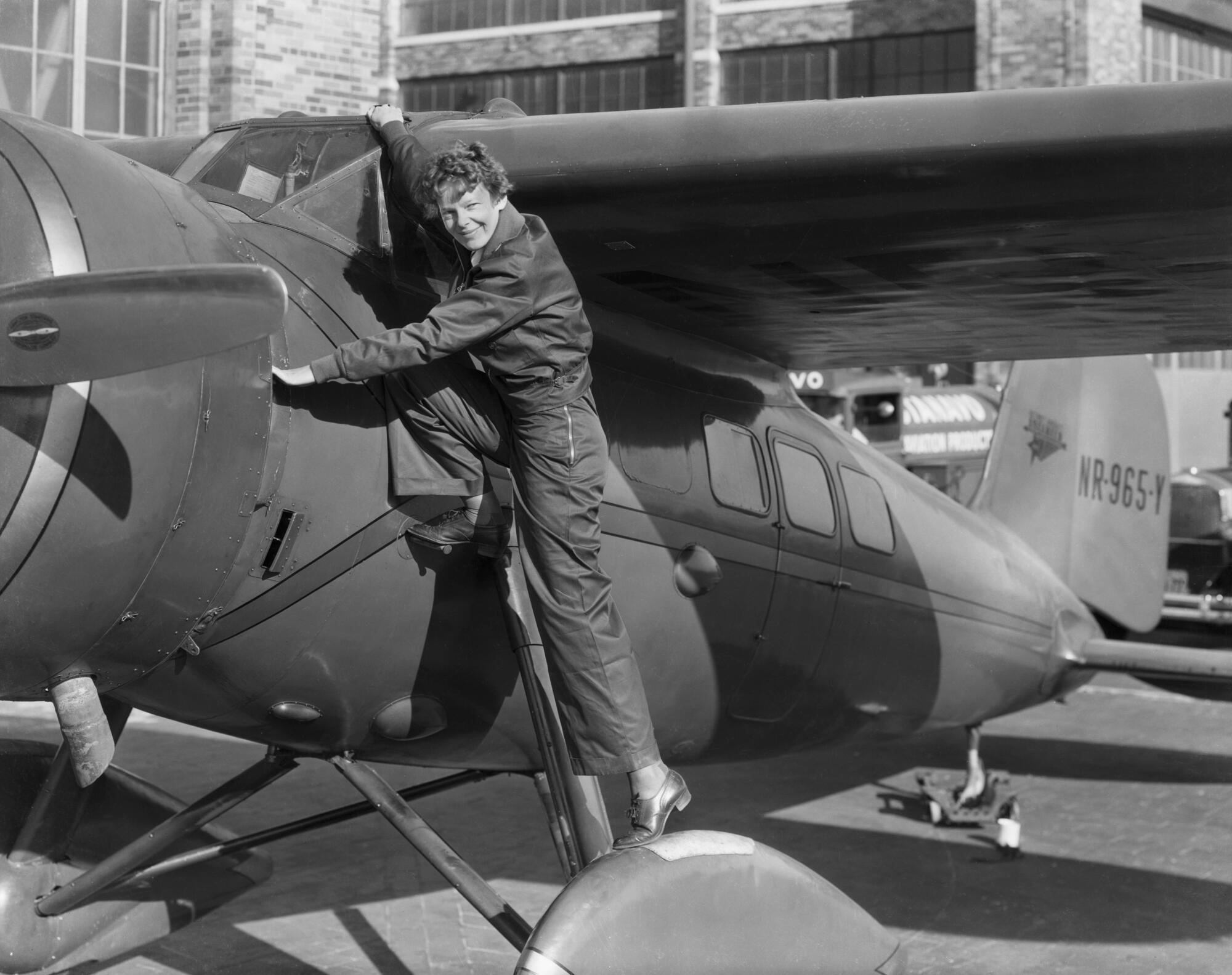 Amelia Earhart stands at the side of a small plane.