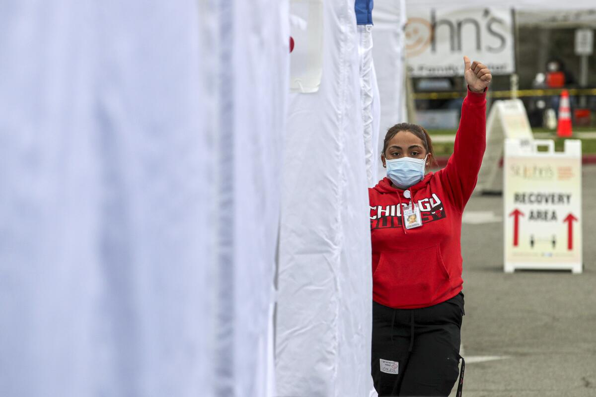 A medical assistant signals to the next patient in line to receive a vaccine at East Los Angeles Civic Center.