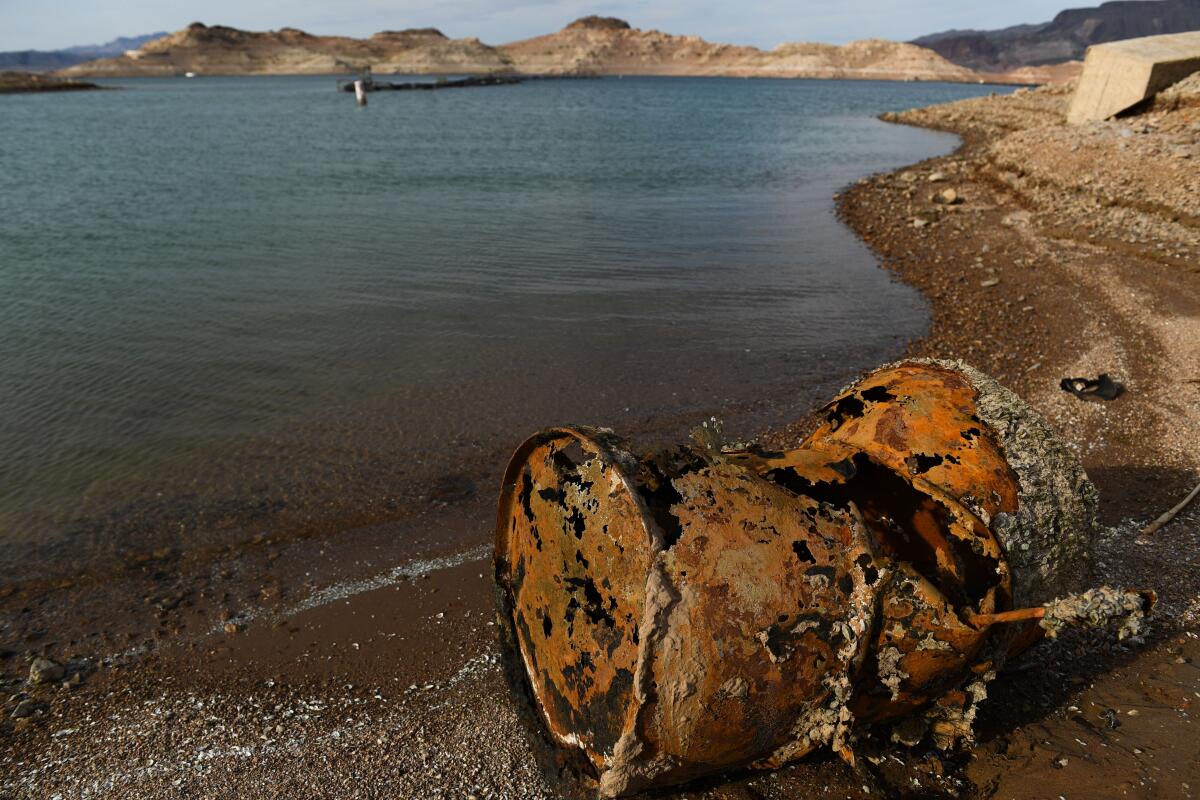 A rusted metal barrel sits exposed on the shore of a lake